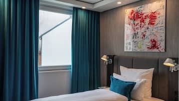 Une chambre d’hôtel moderne avec un grand lit, des rideaux de couleur turquoise, un grand tableau abstrait accroché au mur et deux lampes de chevet.