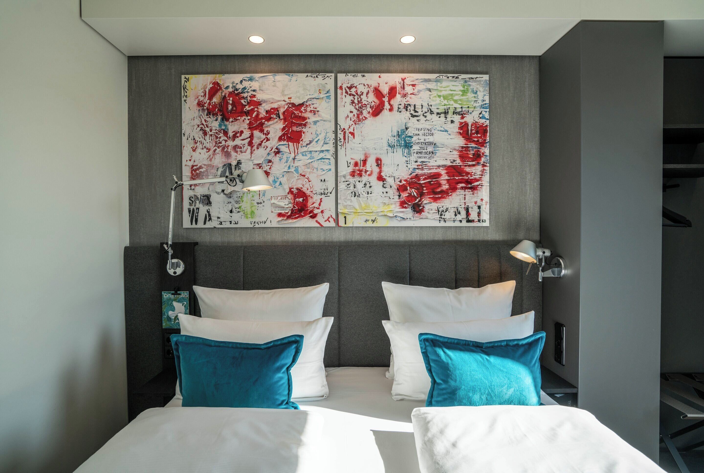 Una camera d'albergo moderna con un letto grande, due cuscini, una testiera e un'opera d'arte appesa al muro.
