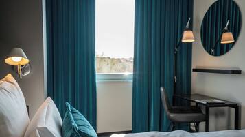 Une chambre d’hôtel avec un lit, un bureau, deux lampes et une vue par la fenêtre, qui est dotée de rideaux.