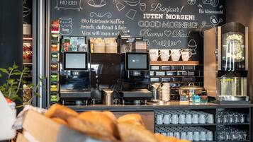 Una cafetería con un menú en pizarra, máquinas de espresso y una exposición de pasteles.