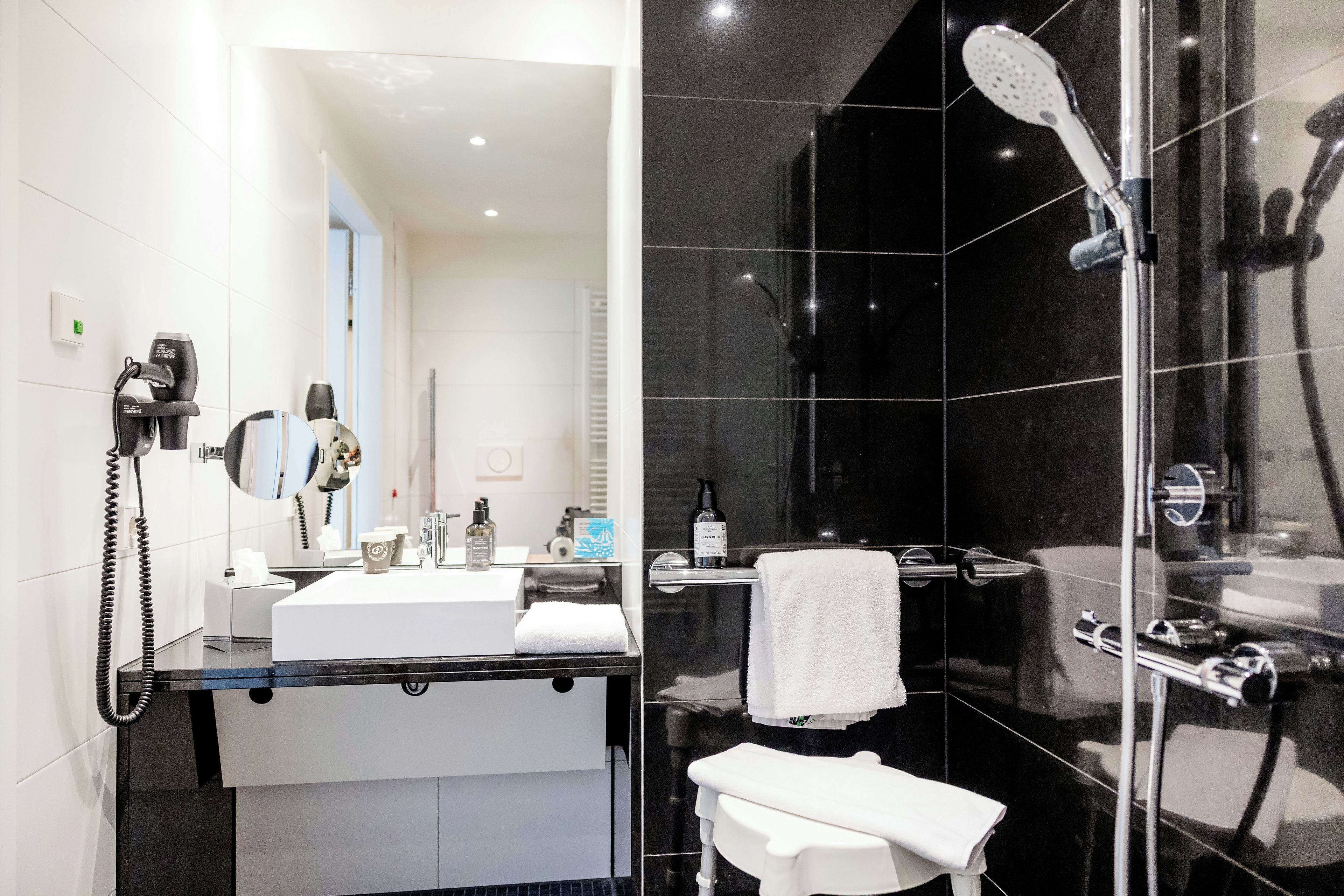 A modern bathroom with a glass shower enclosure, a white sink, and a handheld hair dryer.
