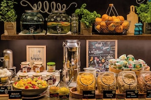 A buffet area with various food options including fruits, salads, and cereals.