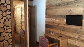 A wooden interior with a TV mounted on the wall, a wooden desk with a chair, and a mirror with a wood log design.
