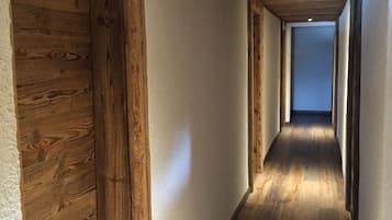 A narrow hallway with wooden beams on the ceiling and walls, leading to a door at the end.