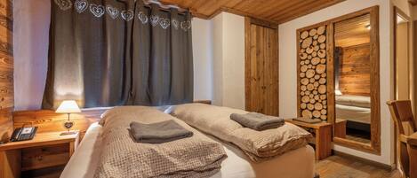 A wooden cabin-style bedroom with two beds, a nightstand with a lamp, and a wooden wall with logs.