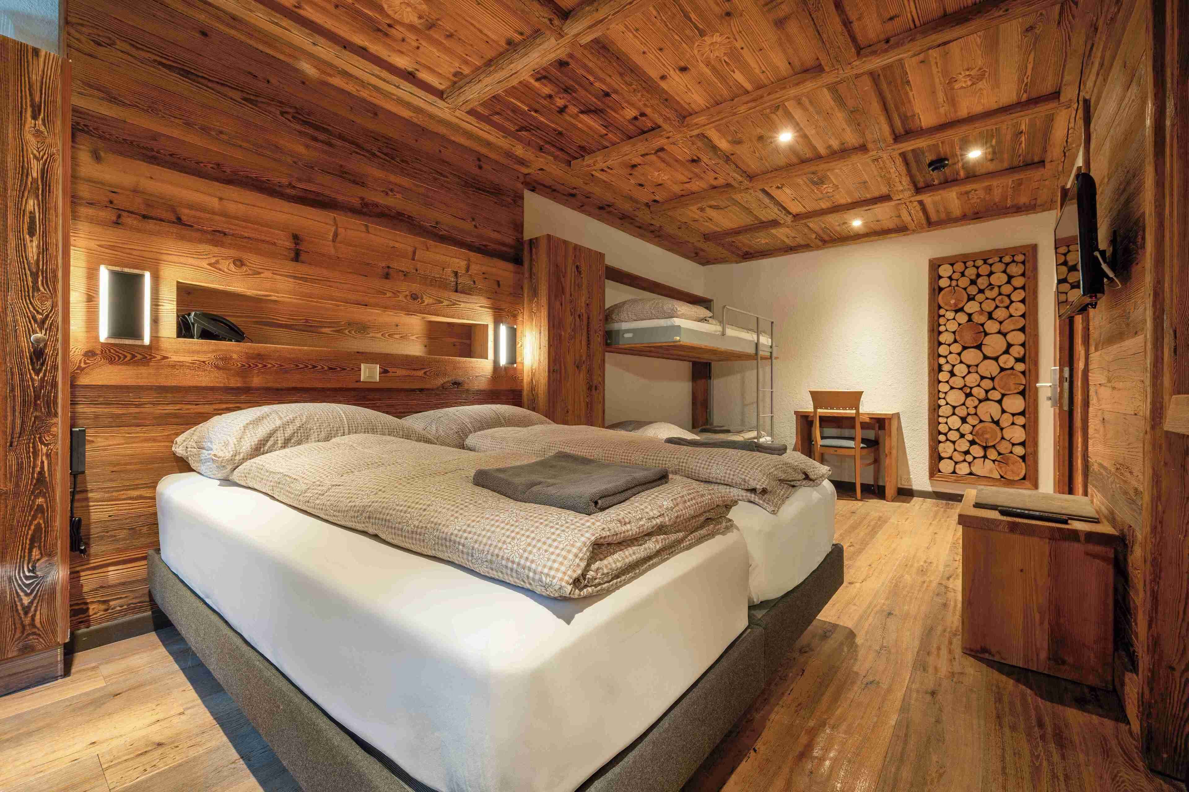 A wooden cabin bedroom with bunk beds, a small table, and a wall-mounted shelf.