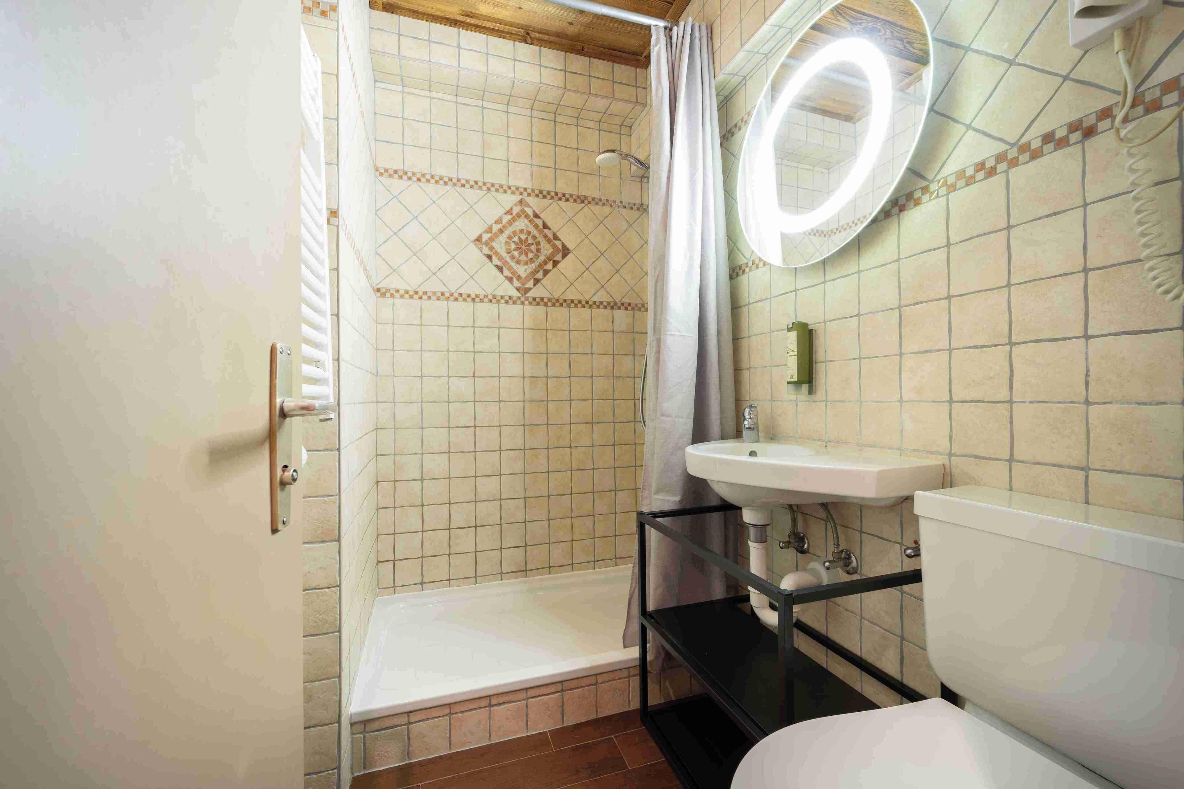 A bathroom with a shower, toilet, sink, and a mirror with a light.