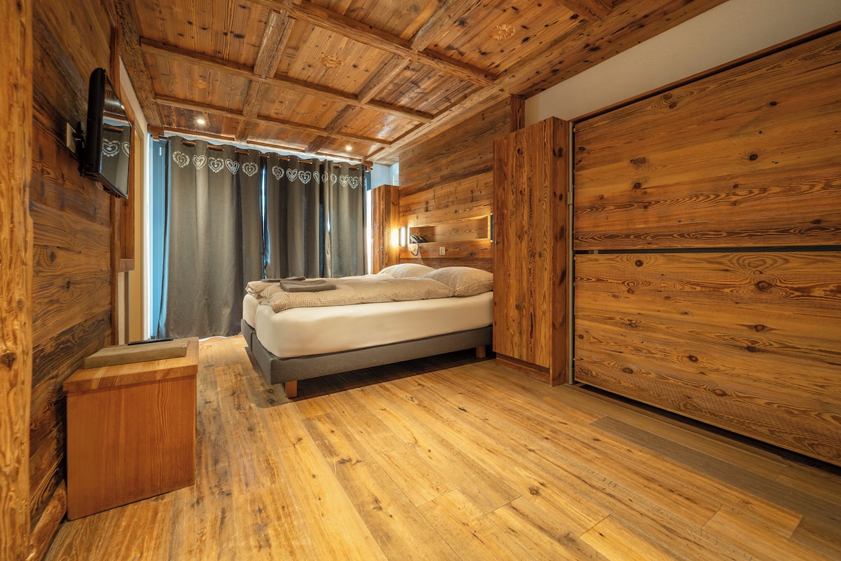 Un dormitorio con paneles de madera, una cama, cortinas y un televisor montado.