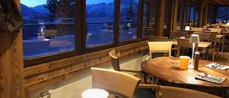 Un restaurante acogedor con interiores de madera y ventanas amplias que ofrecen vistas a un paisaje nevado.
