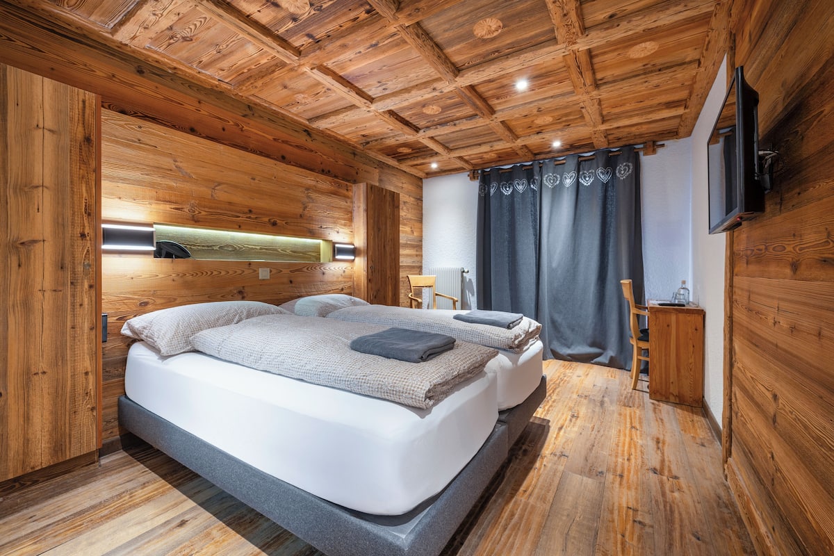 Una habitación con paneles de madera, una cama, un televisor y una ventana con cortinas.