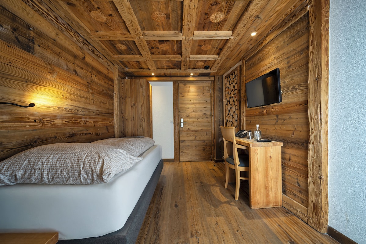 Una habitación de cabaña de madera con una cama, un escritorio y un televisor montado en la pared.