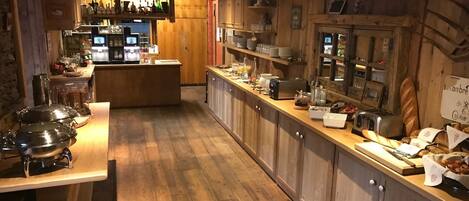 A rustic kitchen with wooden cabinets, a central island with appliances, and a bar area in the background.