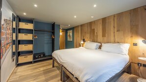A bedroom with a bed, wooden wall paneling, a wardrobe with open doors, and a wall-mounted lamp. - Grassmarket hotel (Edinburgh)