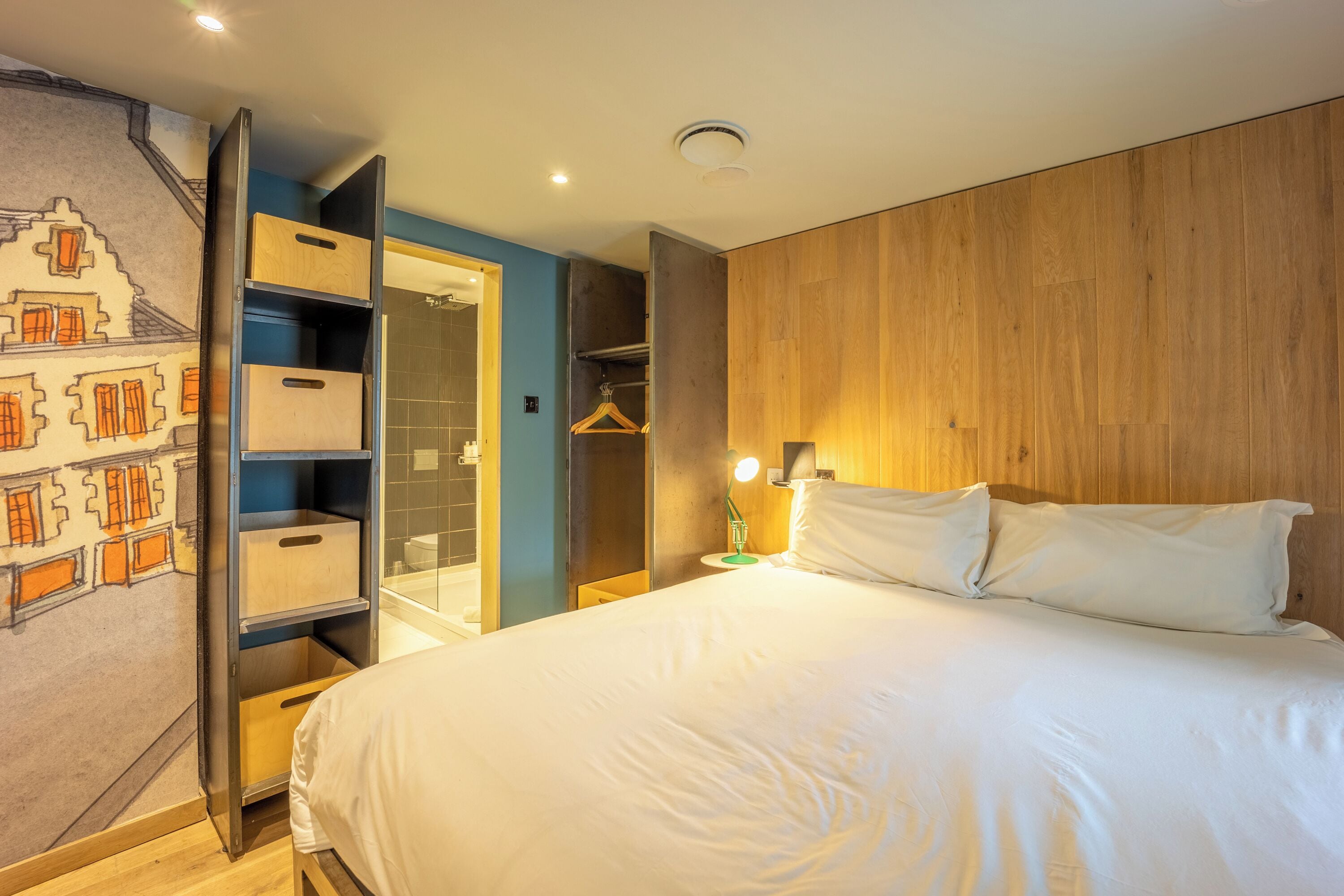 Une chambre à coucher comprenant un lit, une armoire, un portant et un mur orné d’une fresque.