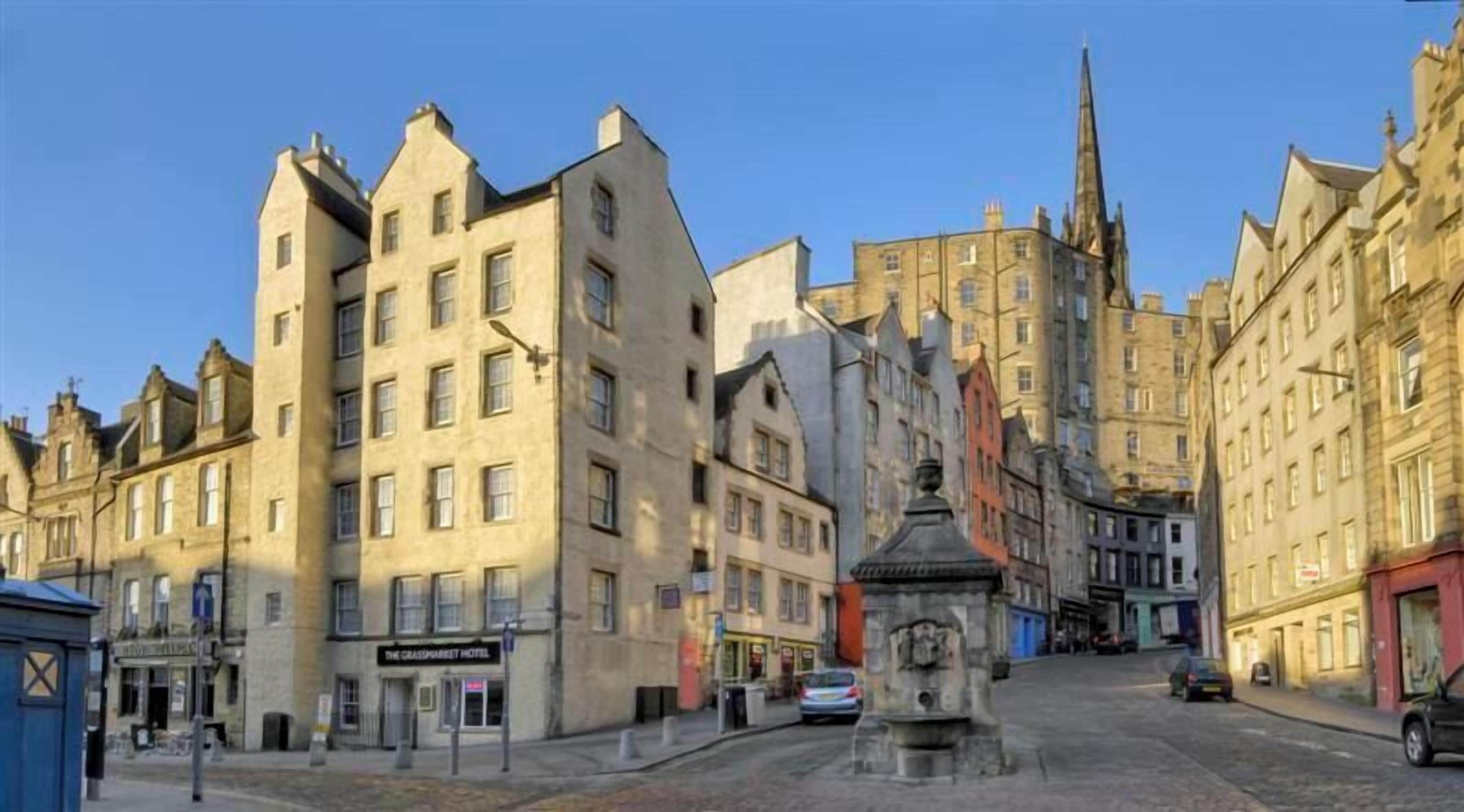 A historic street with traditional architecture, including a prominent church spire and a central fountain.