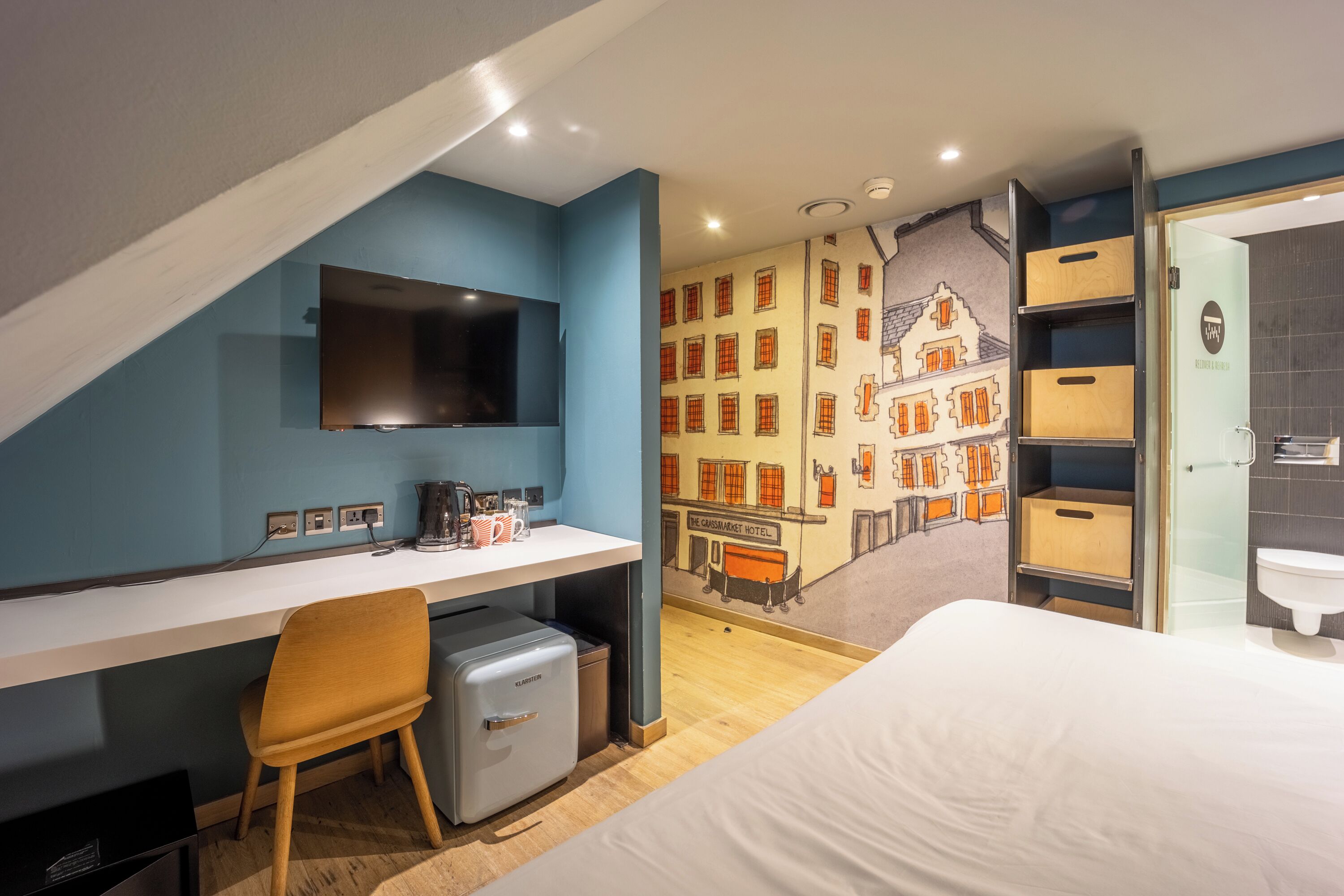 A modern hotel room with a desk, chair, flat-screen TV, and a mural of a building.