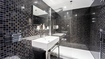 Ein modernes Badezimmer mit einem großen Spiegel, zwei Waschbecken, einer Badewanne und schwarzen Fliesen.