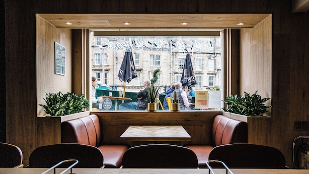A restaurant with wooden walls, a large window with a view of the street, and seating arrangements including booths and tables. - Grassmarket hotel (Edinburgh)