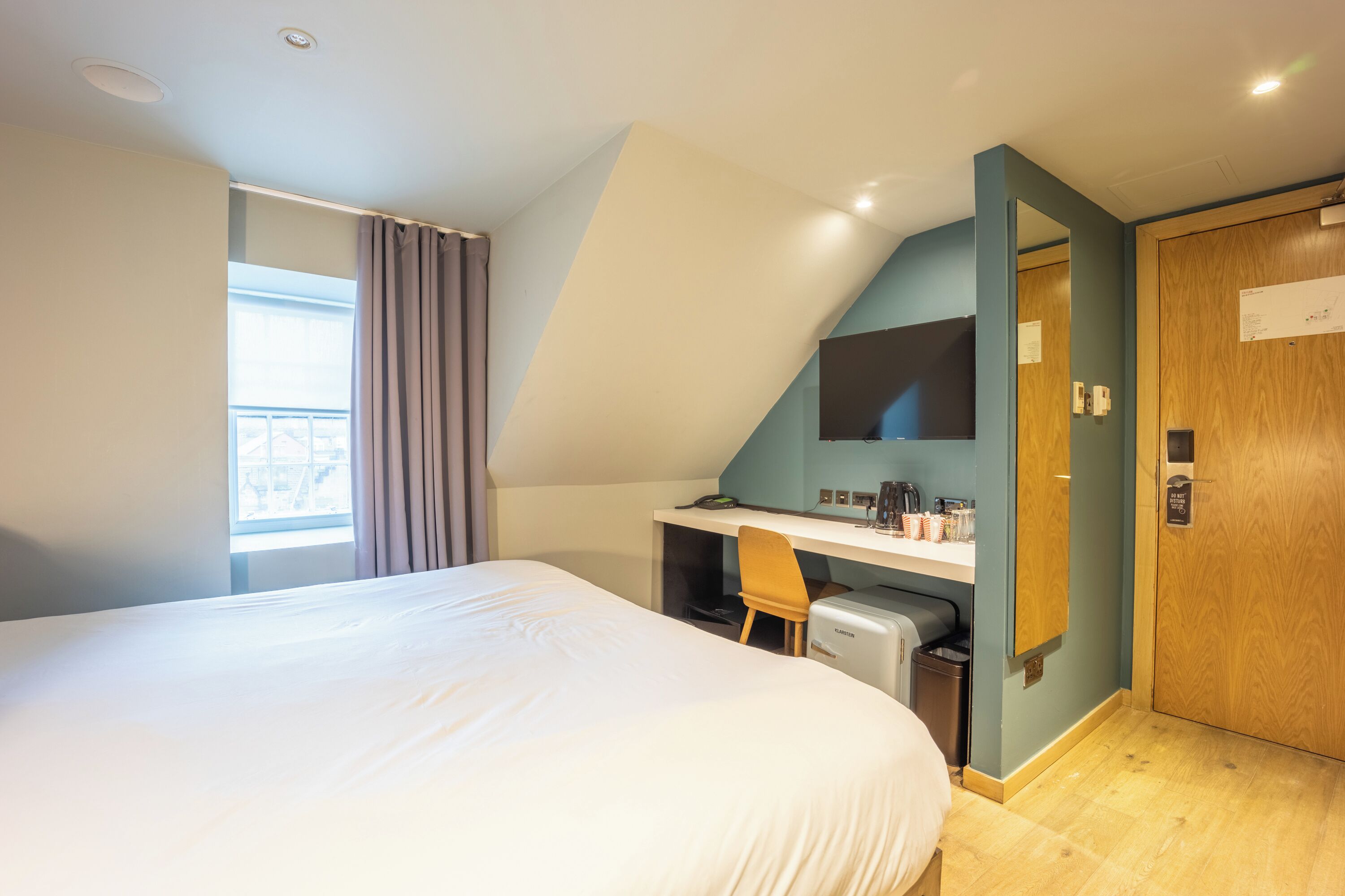 Een slaapkamer met een groot bed, een bureau met stoel, een televisie en een deur.