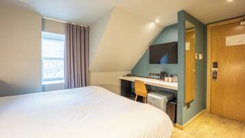 Een slaapkamer met een groot bed, een bureau met stoel, een televisie en een deur.