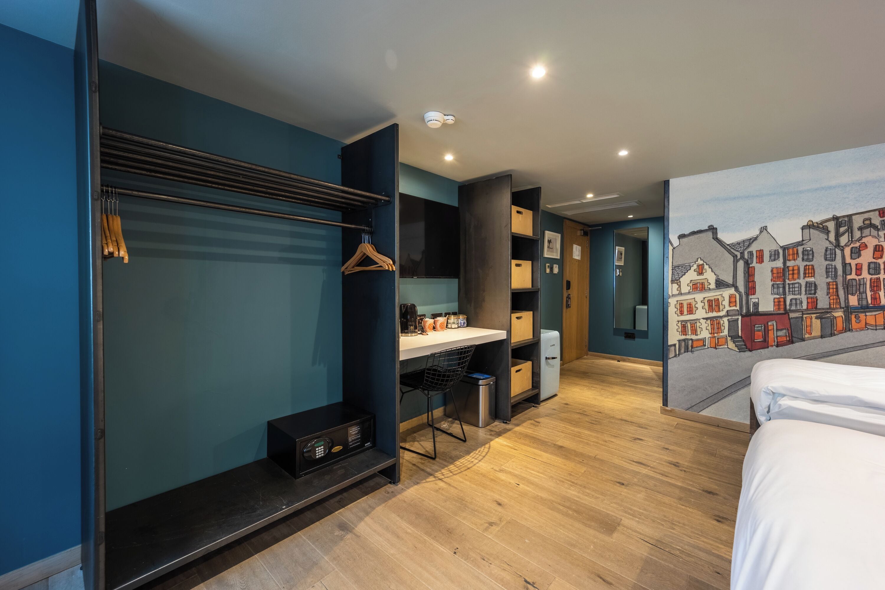 A modern hotel room with a bed, a desk, a chair, and a wardrobe.
