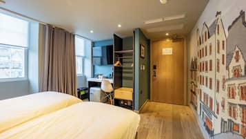 Hotellihuone, jossa on kaksi sänkyä, työpöytä, tuoli, vaatekaappi ja seinämaalaus, jossa on kuvattu rakennuksia.