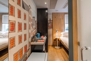 A hotel room with a bed, a desk with a lamp, and a wall with a cityscape mural.