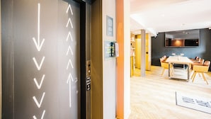 A hotel lobby with a modern design, featuring a reception desk, a seating area, and directional arrows on the elevator doors. - Grassmarket hotel (Edinburgh)