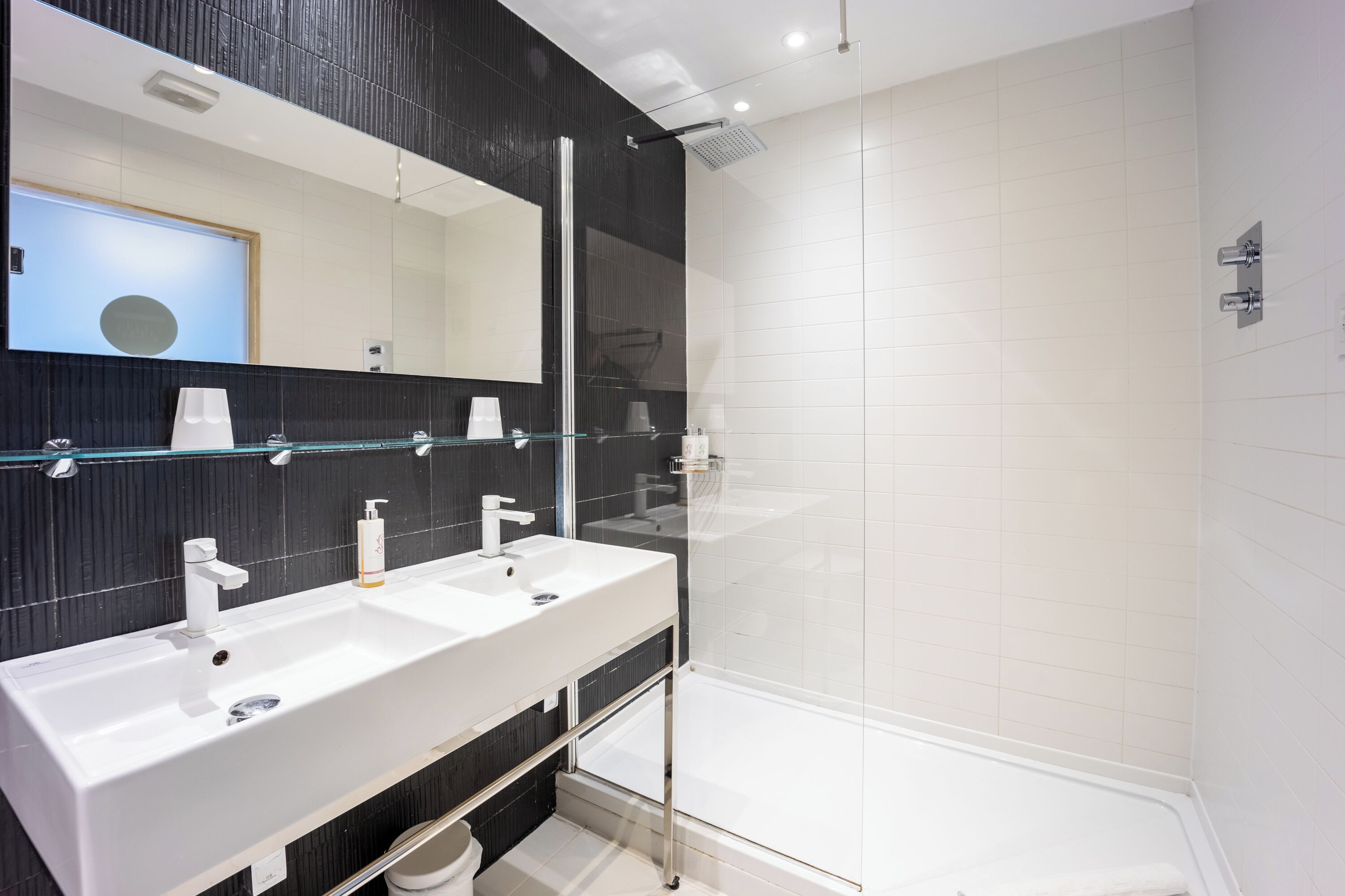 Un baño moderno con dos lavamanos, un espejo grande y ducha con mampara de vidrio.
