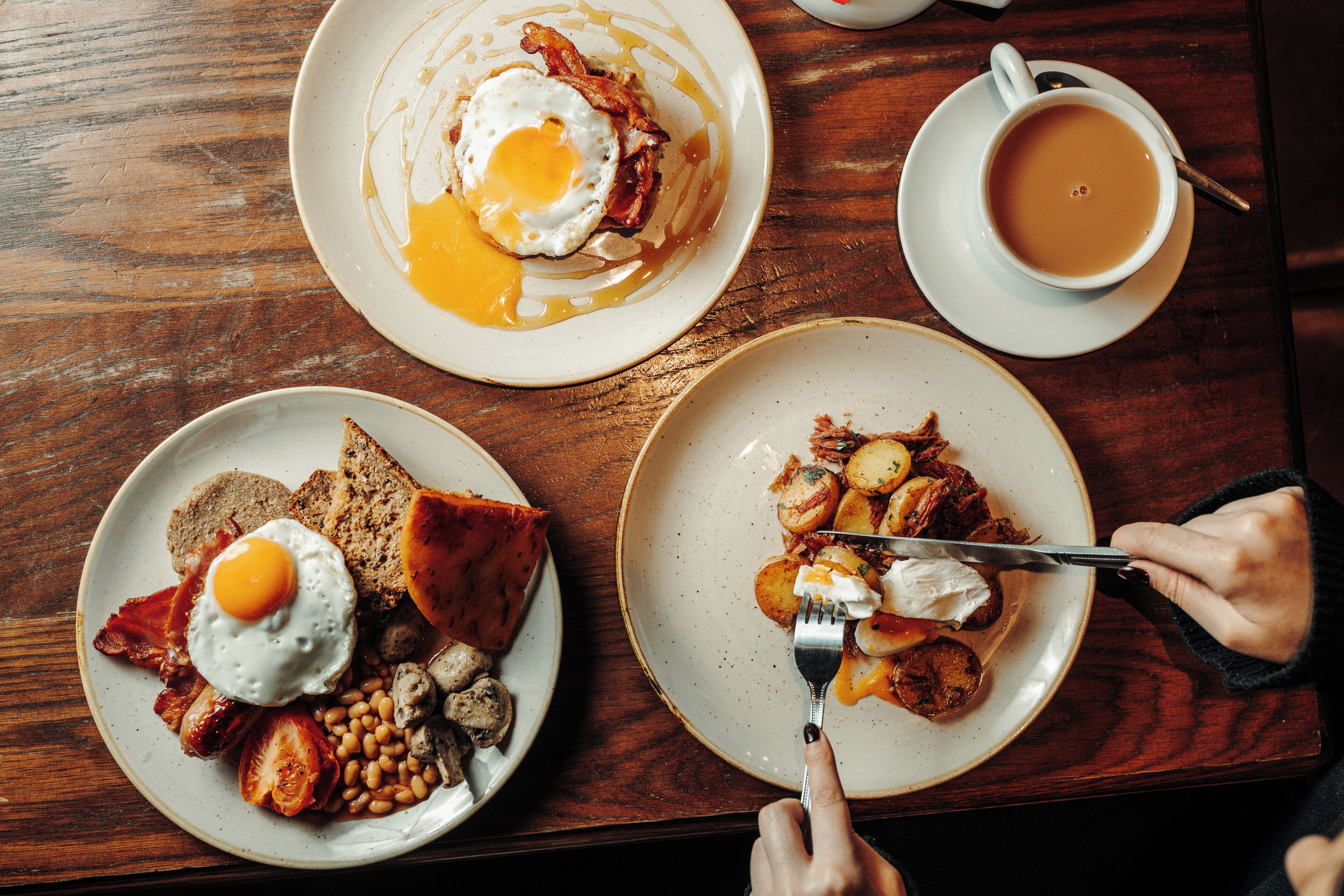Une table en bois sur laquelle sont disposées des assiettes de petit-déjeuner contenant des œufs, du bacon, des toasts, des haricots, des champignons et des pommes de terre.