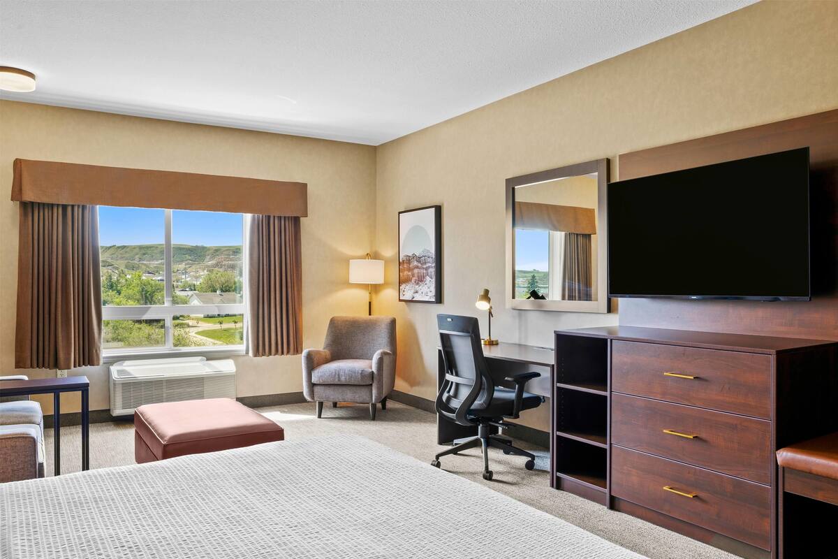 Una habitación de hotel con cama, escritorio, silla, televisión y ventana con cortinas.