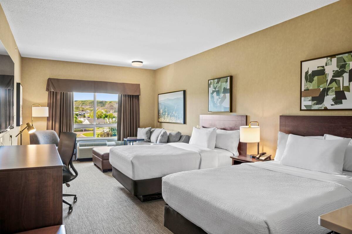 Habitación de hotel con dos camas, un escritorio, una silla y vistas a un paisaje urbano.