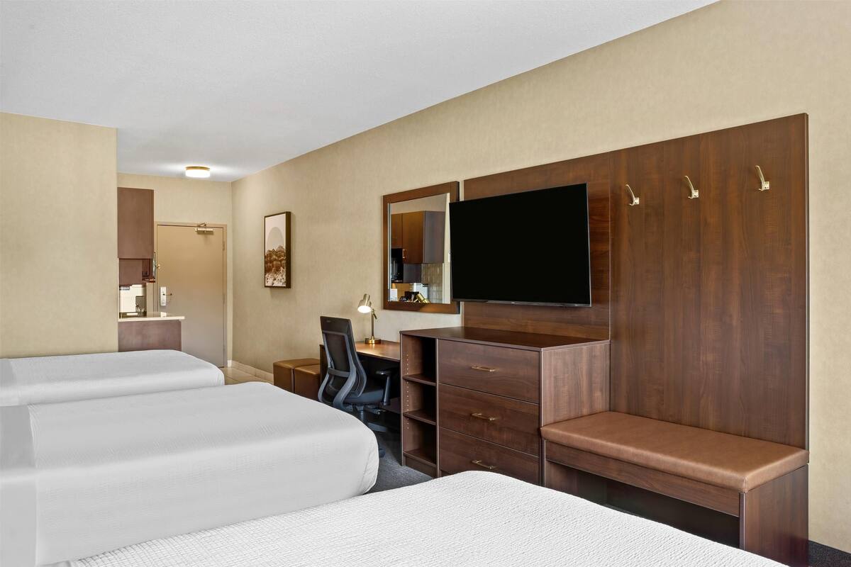 Una habitación de hotel con dos camas, un escritorio, una silla, un televisor y un armario.