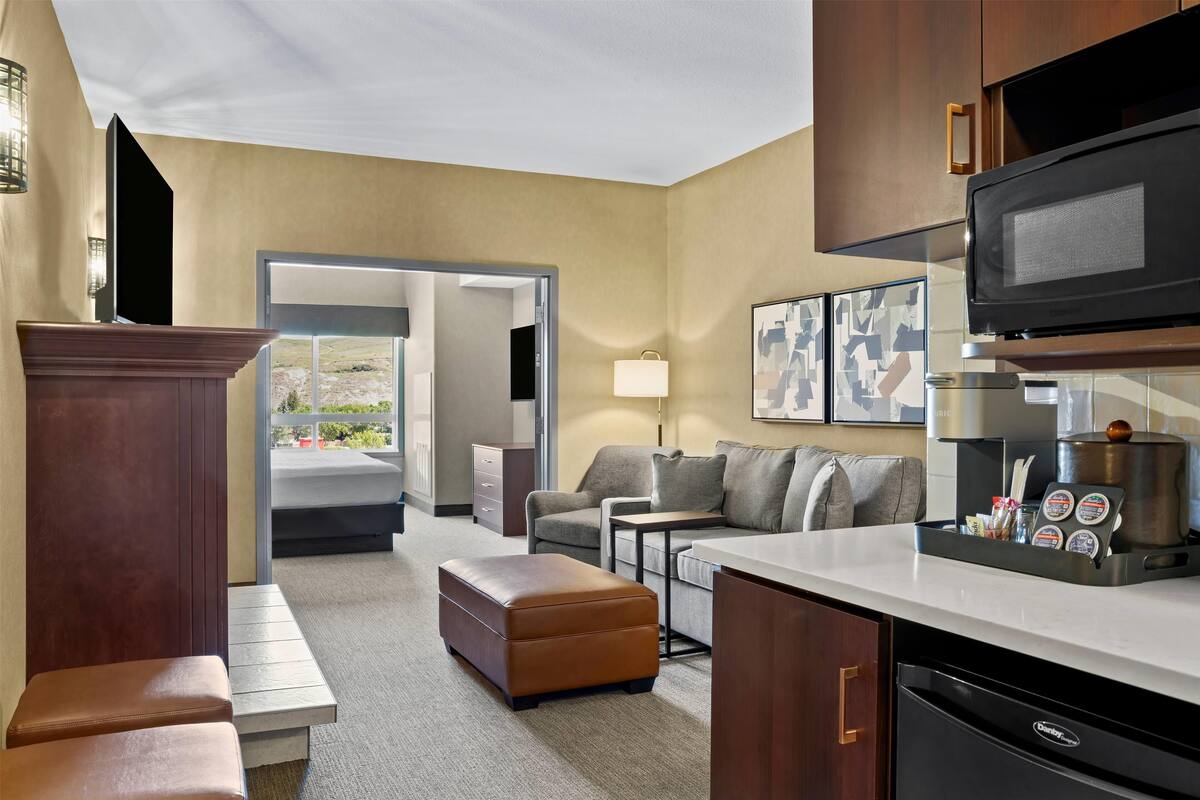 Una habitación de hotel moderna con kitchenette, un sofá, una mesa de centro y vistas al exterior.
