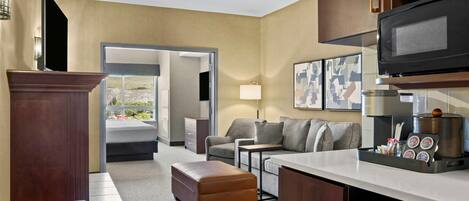 A modern hotel room with a kitchenette, a sofa, a coffee table, and a view of the outdoors.