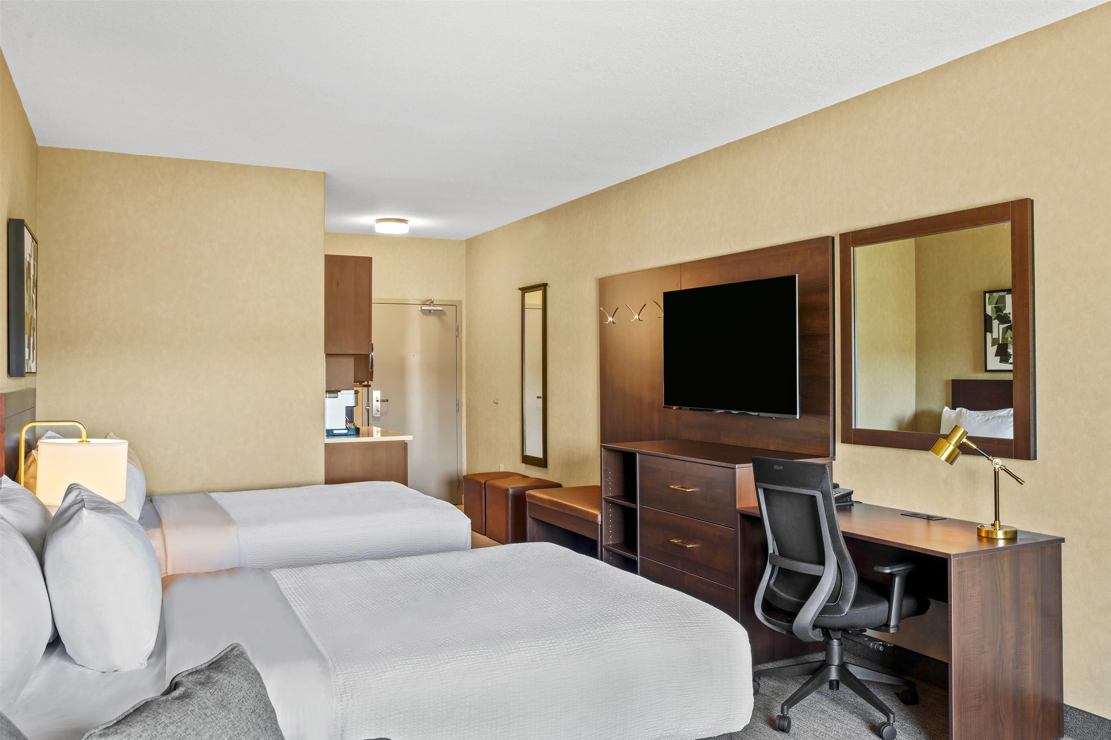 A hotel room with two beds, a desk, a chair, a TV, and a mirror.