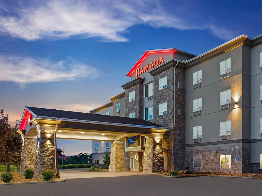 Ein Ramada Hotel mit modernem Design, das eine Steinfassade, zahlreiche Fenster und einen überdachten Eingangsbereich aufweist.