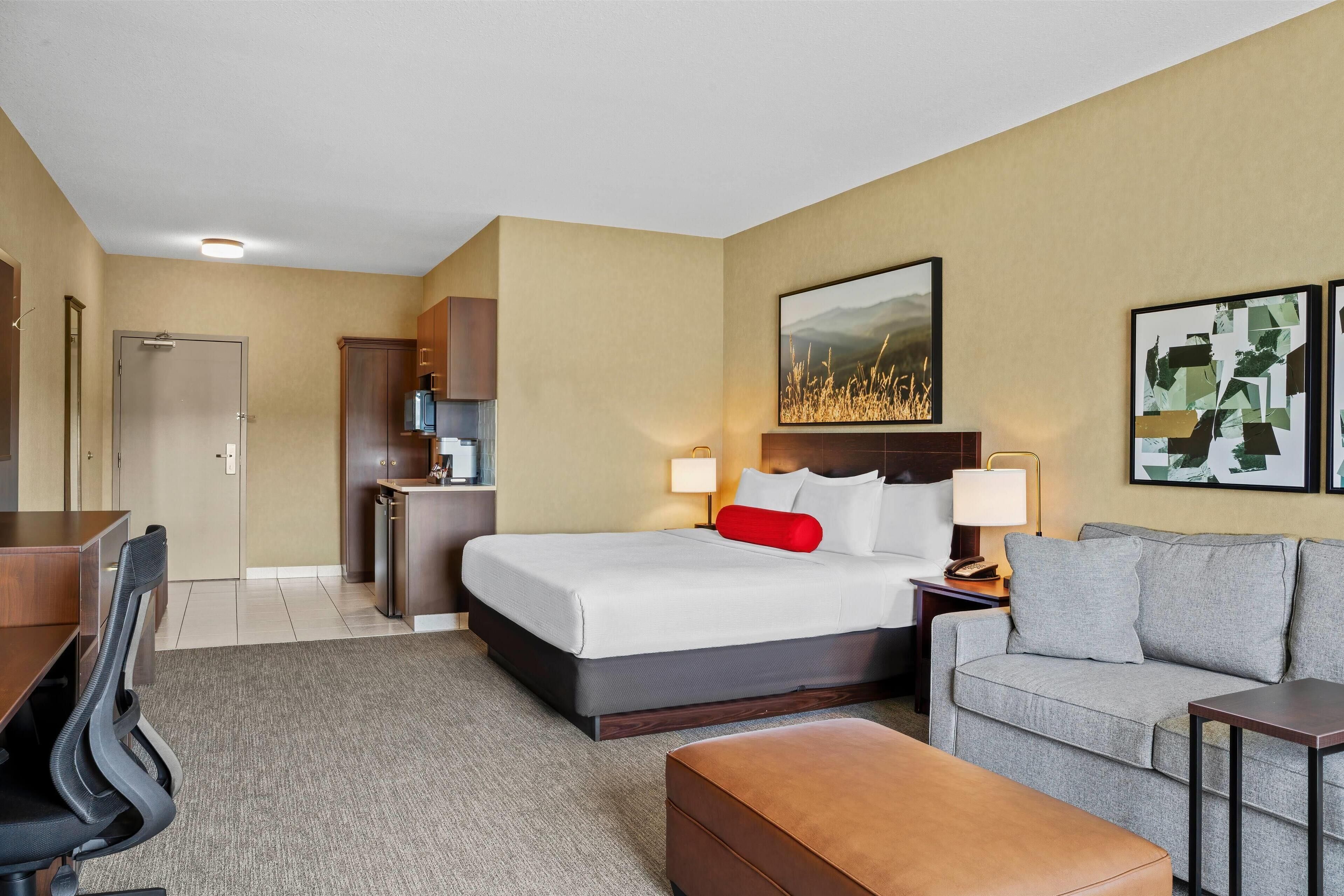 Una habitación de hotel con cama, sofá, escritorio y kitchenette.