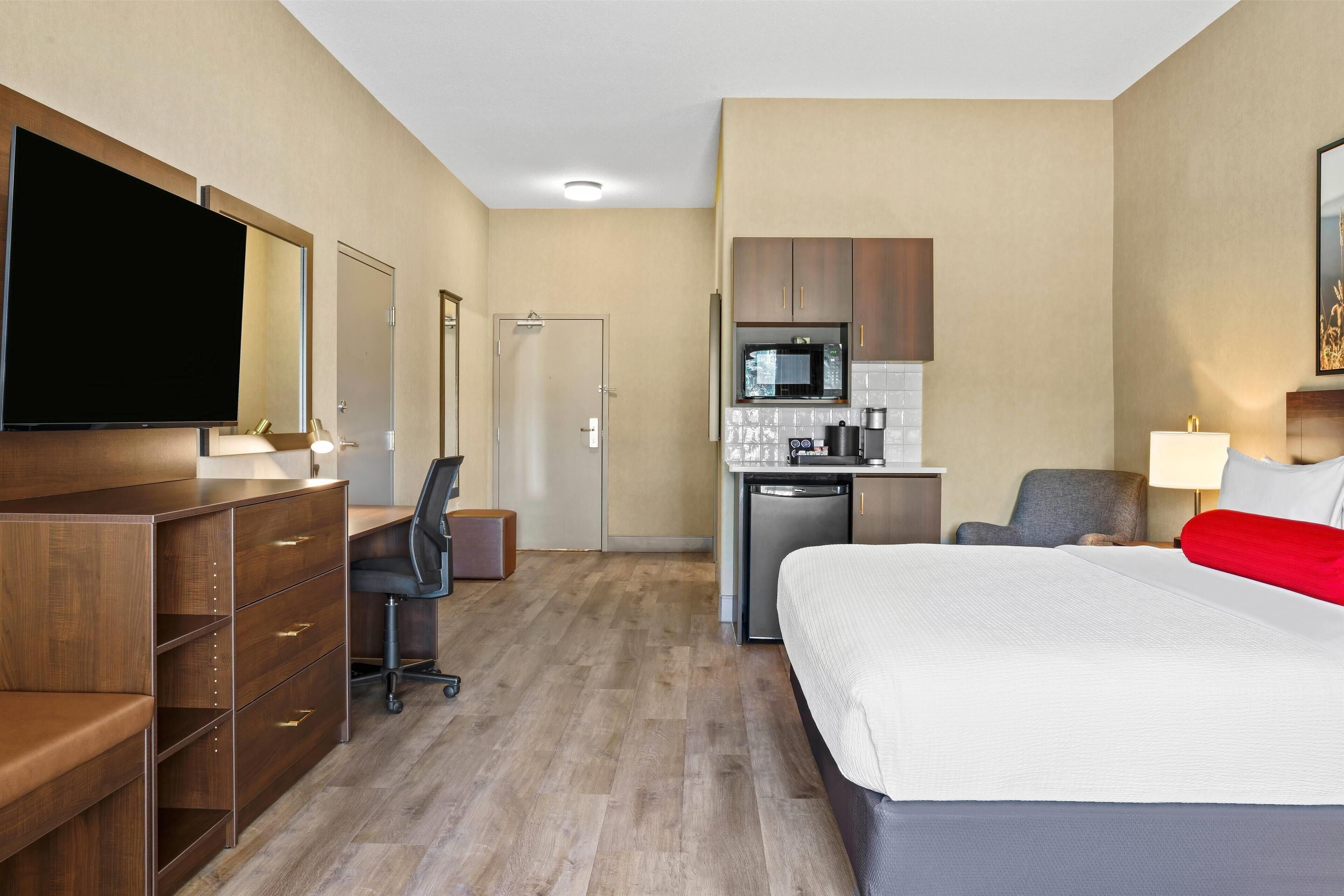 Ein Hotelzimmer mit Bett, Schreibtisch, Küchenzeile und Fernseher.