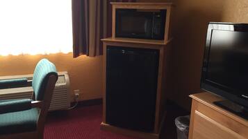 A hotel room with a single bed, a desk, a microwave, a television, and a small refrigerator.