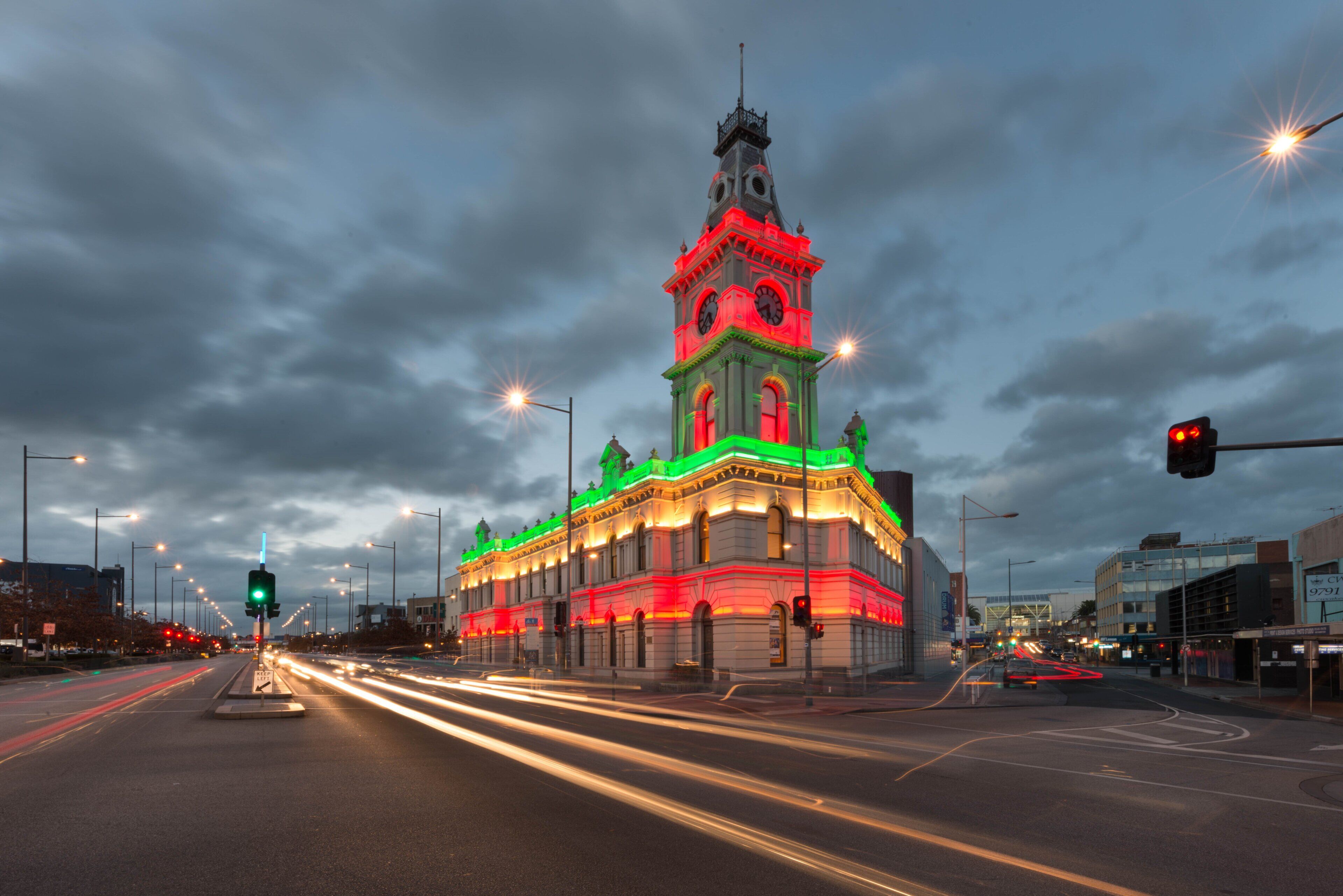 Un bâtiment historique doté d’une tour horloge, entouré de lampadaires et de feux de signalisation modernes.
