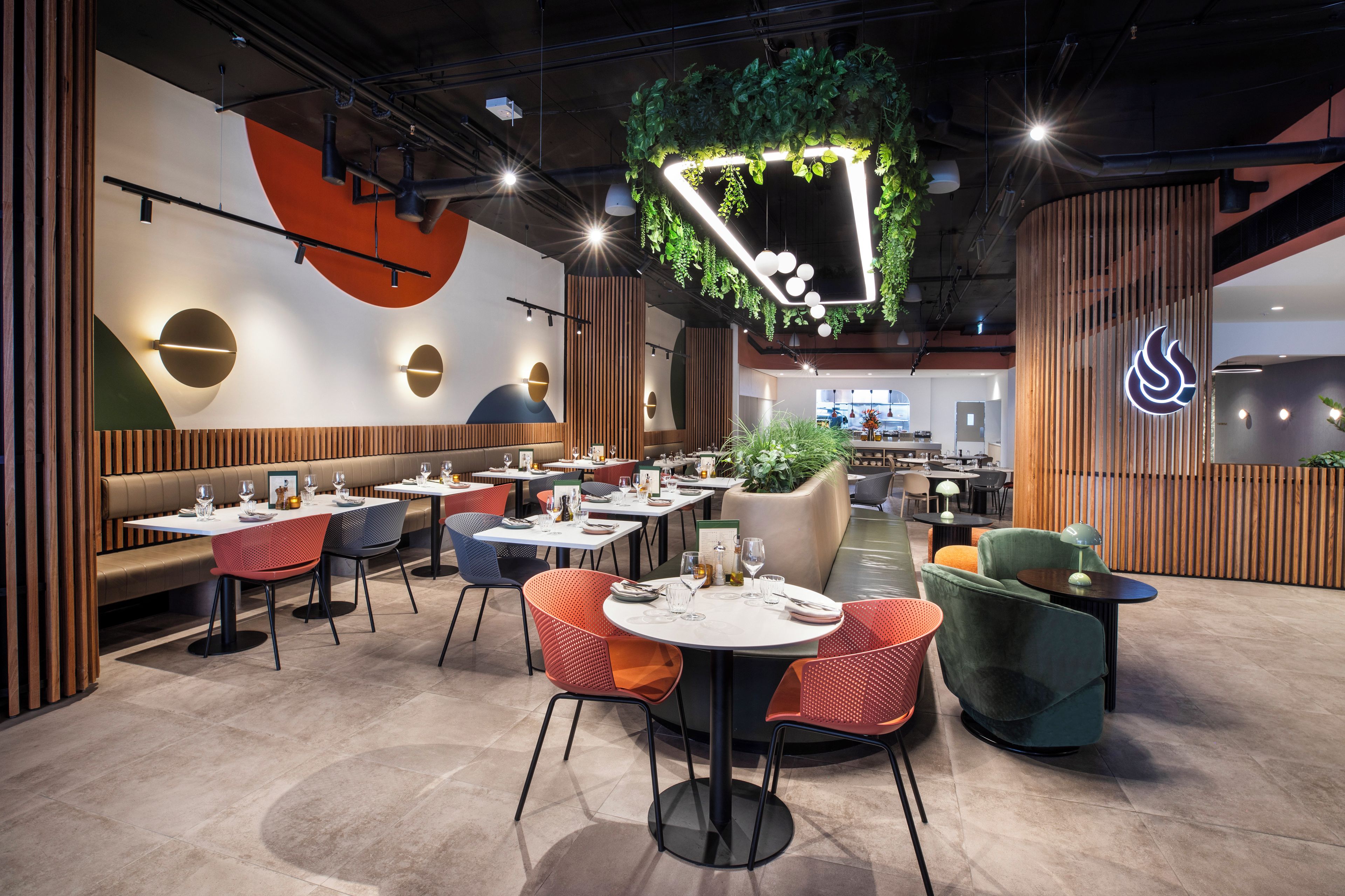 A modern restaurant interior with booths, round tables, and a central green plant installation.