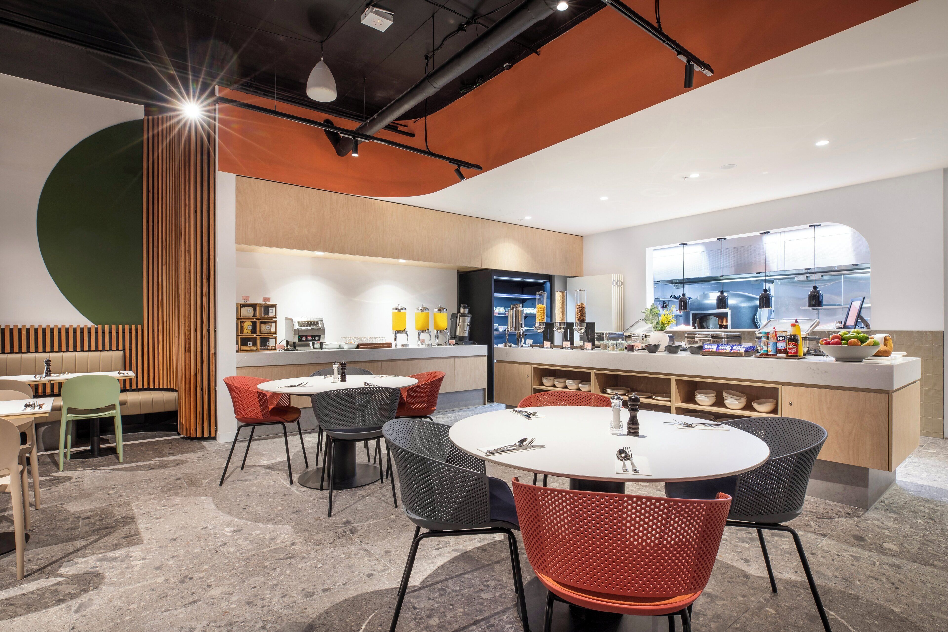 A modern restaurant with round tables and chairs, a bar area, and a visible kitchen.