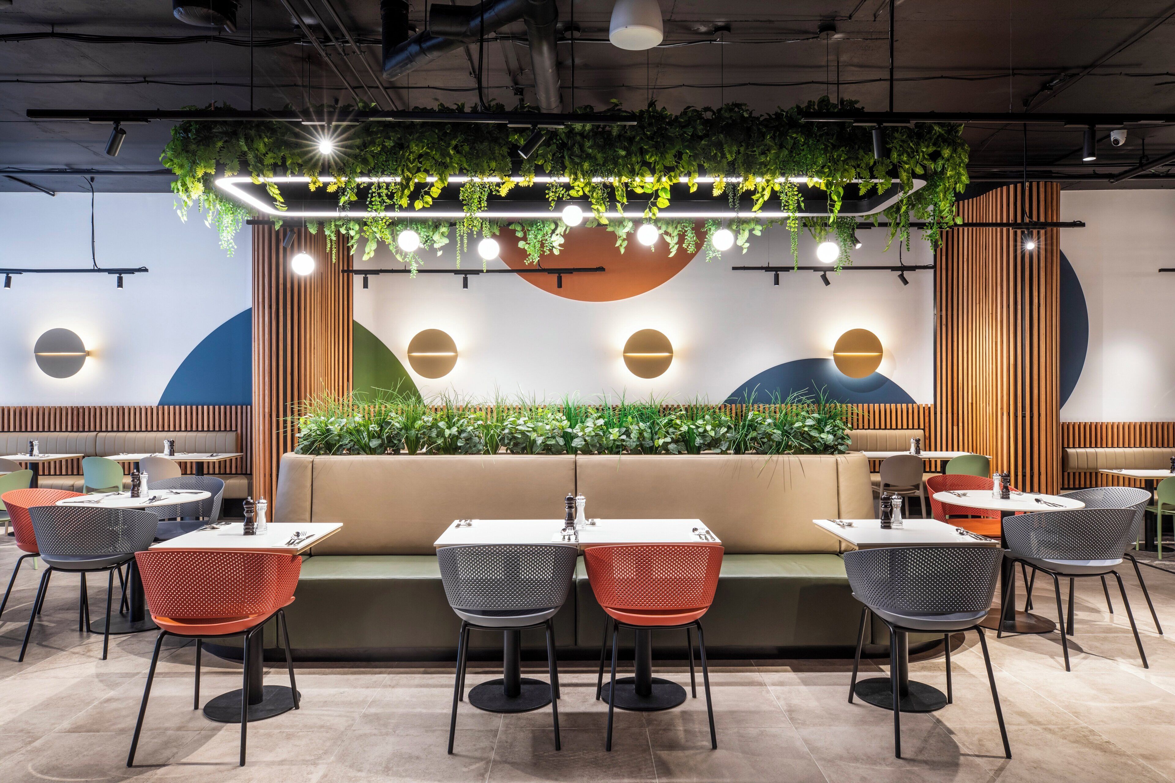 Een modern restaurantinterieur met ronde tafels, rode en zwarte stoelen en een centraal zitgedeelte met een plantenbak.