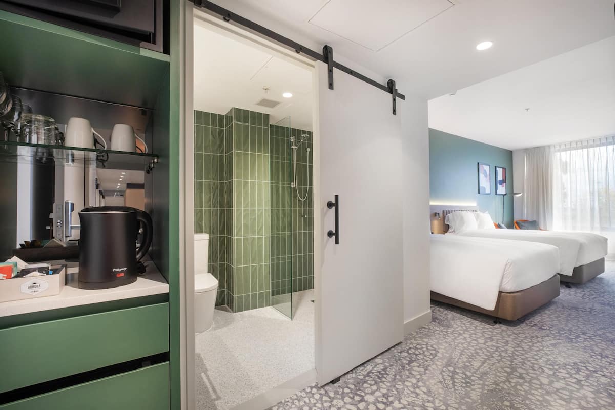 Une chambre d’hôtel dotée d’une porte coulissante donnant accès à une douche, d’un lit, d’une table de chevet et d’une machine à café posée sur le comptoir.