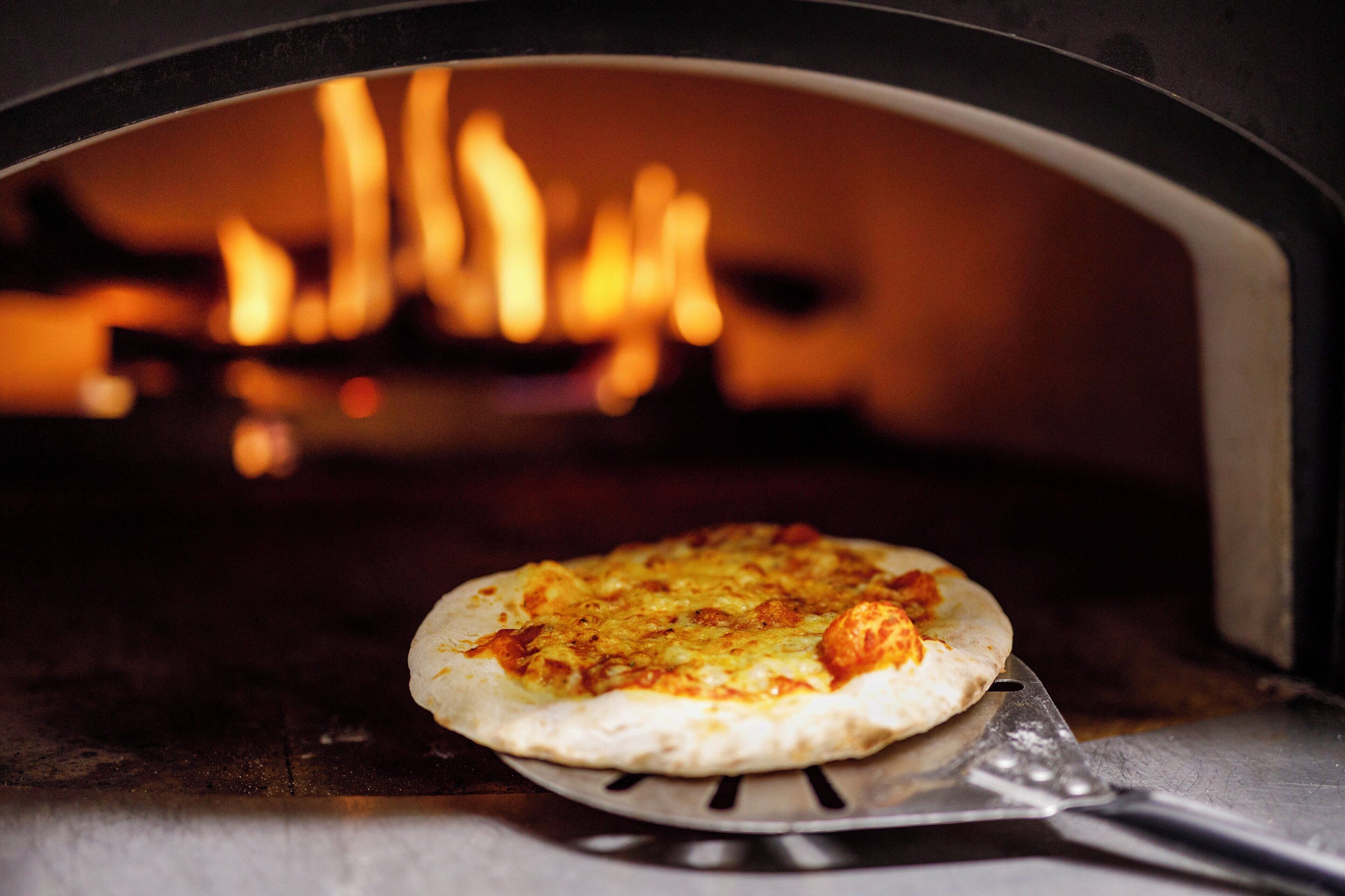 A pizza inside a wood-fired oven with visible flames.