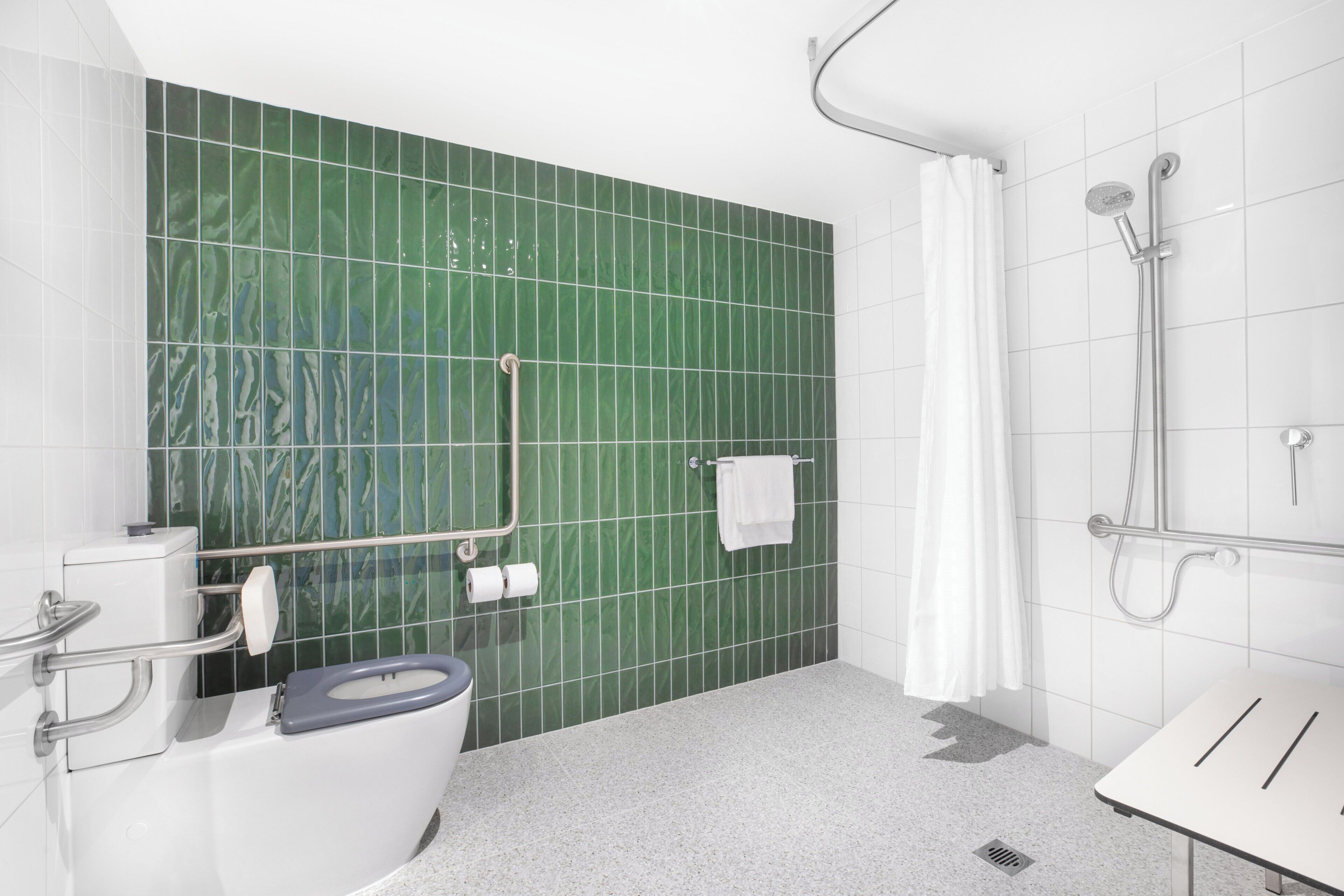 A bathroom with a green tiled wall, a white toilet, a shower area with a curtain, and a sink with a towel rack.