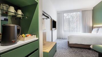 A hotel room with a bed, a coffee maker, a desk with a cup holder, and a window with curtains.