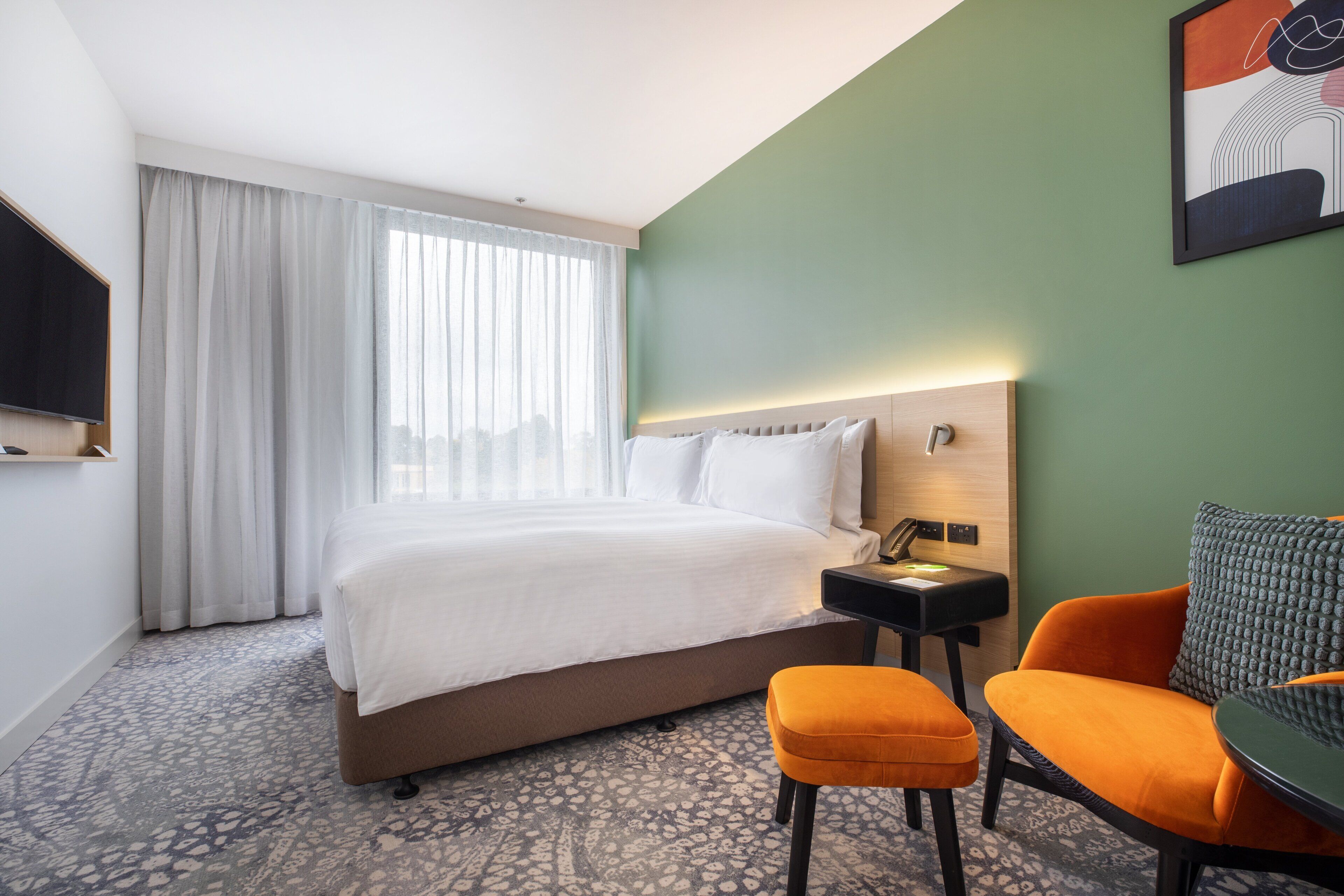 Una habitación de hotel con una cama, un escritorio, una silla naranja y un televisor.