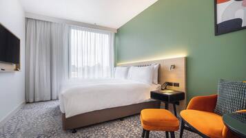 Una habitación de hotel con una cama, un escritorio, una silla naranja y un televisor.